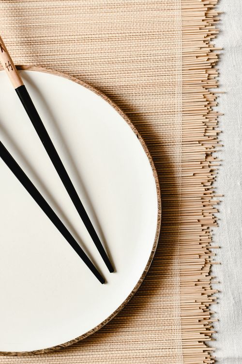 Free An overhead shot of chopsticks on a white plate with a bamboo mat and neutral tones. Stock Photo