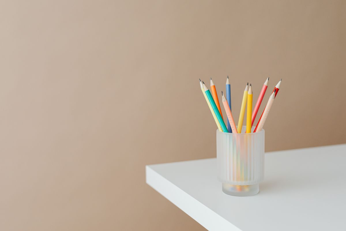 Colored pencils in a frosted glass holder on a white table