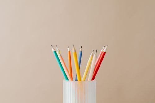 Free Array of multicolored pencils standing upright in a holder against a beige backdrop. Stock Photo