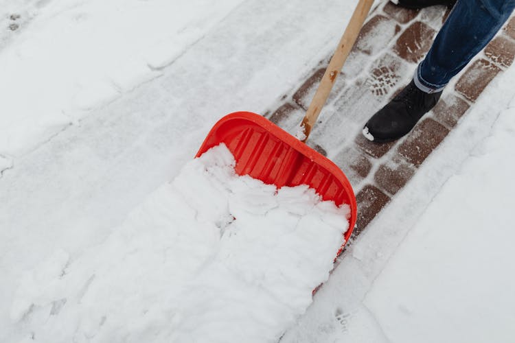 Close-up Of Man Plowing The Driveway With A Red Snow Shovel 