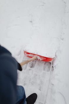 Person shoveling snow from a cobblestone sidewalk with a red shovel in winter.
