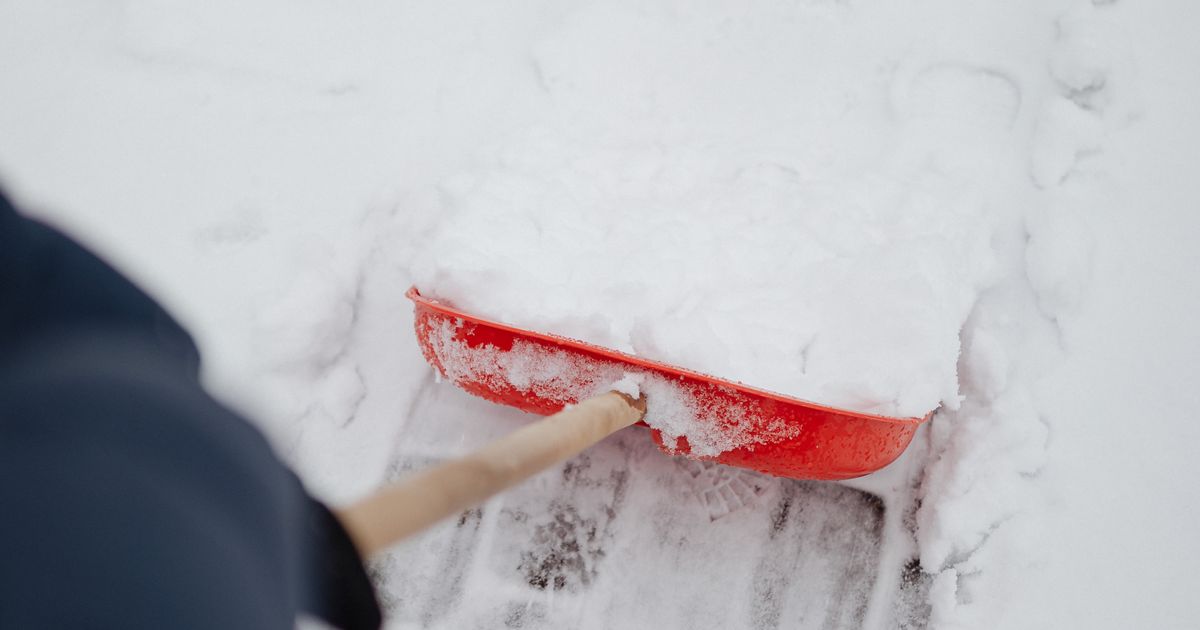 Person schiebt mit einer roten Schaufel Schnee von einem gepflasterten Gehweg, Symbolbild für Winterdienst anbieten