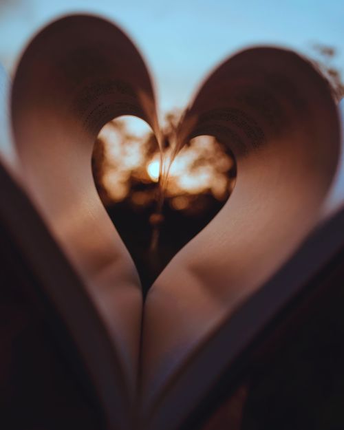 Free A romantic view of sunset through heart-shaped pages of a book, symbolizing love and literary passion. Stock Photo