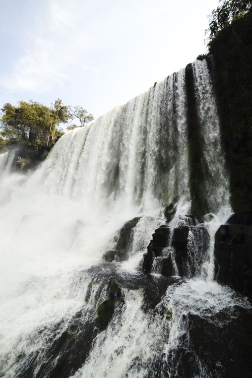 Free Streaming waterfall on cliff with stones spraying water drops against cloudy sky on sunny summer day Stock Photo