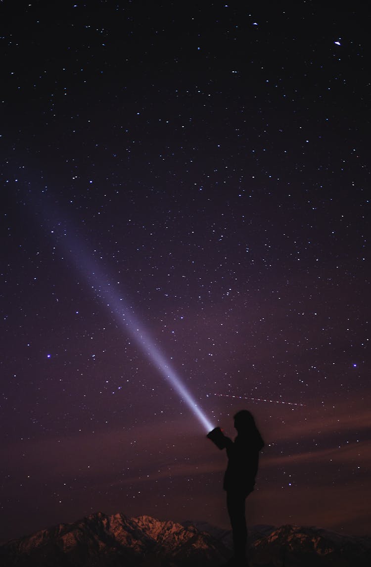 Unrecognizable Traveler With Flashlight Shining In Dark Night Sky