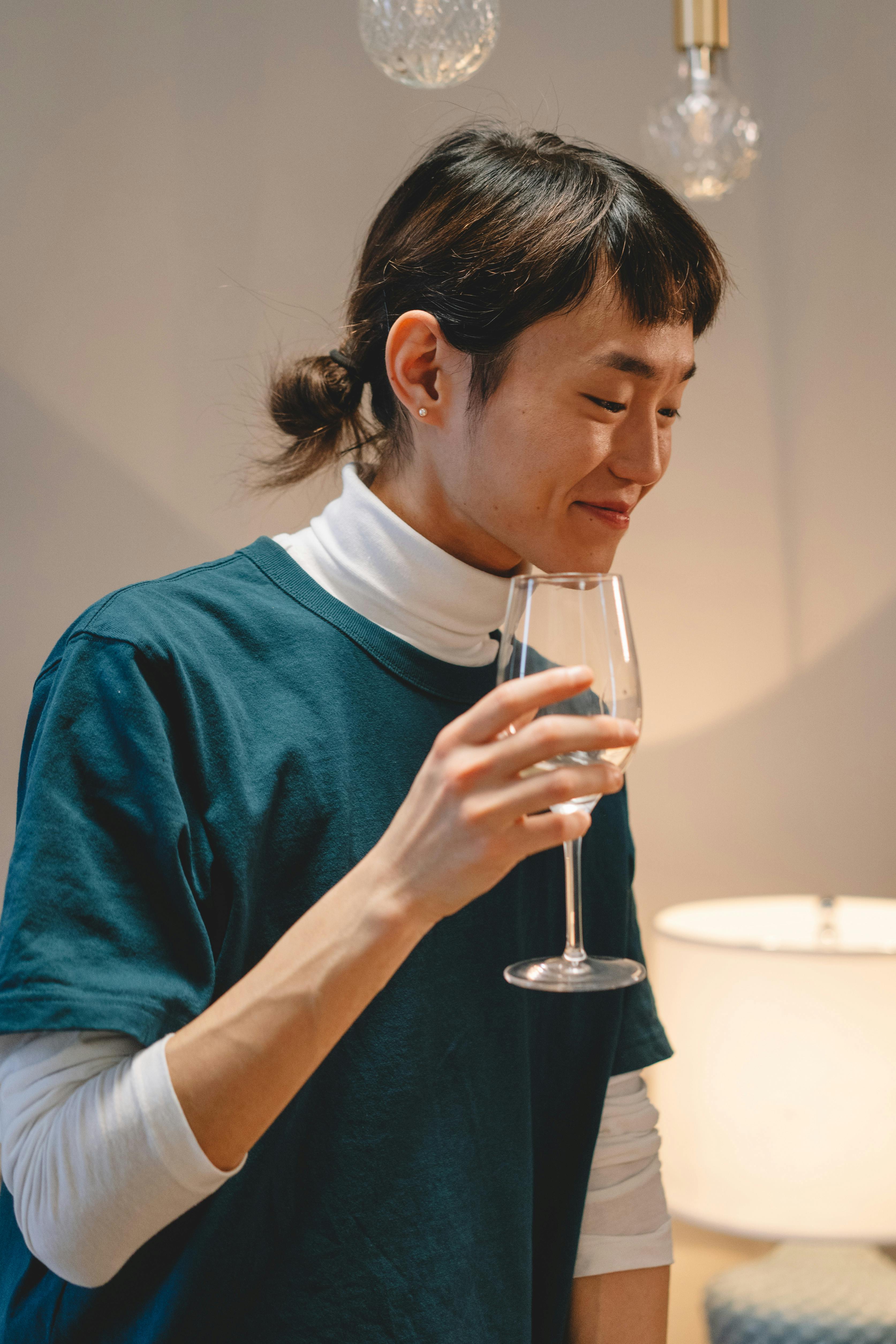 A smiling person enjoys a drink indoors with ambient lighting and a relaxed atmosphere.