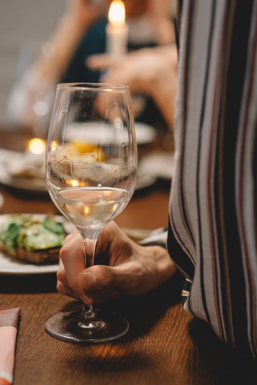 Free Close-up of a hand holding a wine glass at a cozy dinner table indoors. Stock Photo