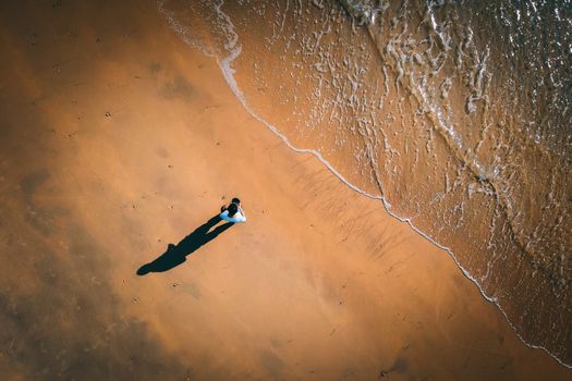 Aerial view of unrecognizable male tourist launching drone standing on sandy beach near wavy sea on sunny day