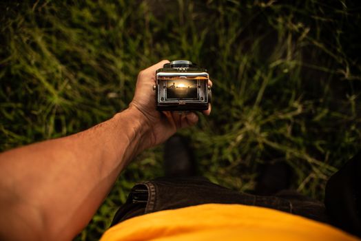 From above of faceless male traveler with twin lens photo camera with screen in hand standing on grassy ground in countryside
