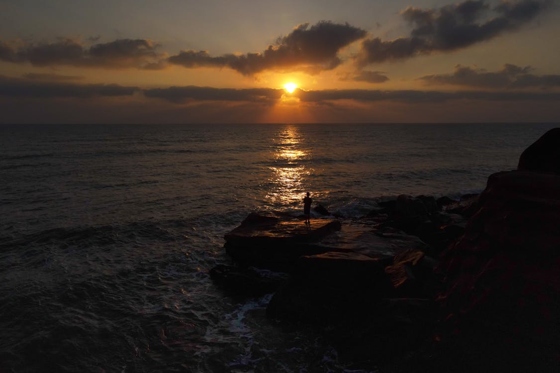 Unrecognizable traveler enjoying sunset over sea from rocky cliff