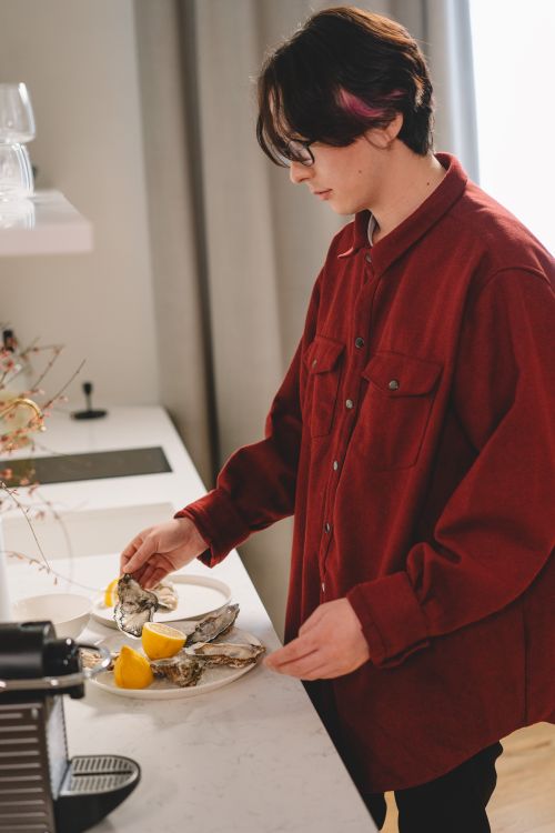 Free An Asian man in a red shirt prepares oysters with lemon in a modern kitchen setting. Stock Photo