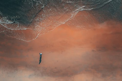 Picturesque drone view of unrecognizable person resting alone on sandy coast ear wavy ocean on sunny day