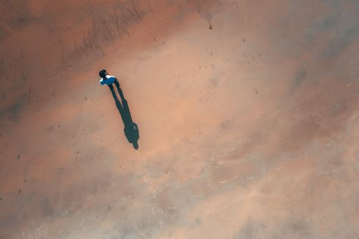 Drone view of unrecognizable male casting shadow on smooth surface of sandy ground