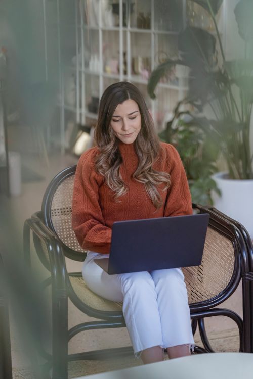 Free Content young female in casual clothes browsing contemporary netbook on laps while sitting on comfy armchair in living room Stock Photo