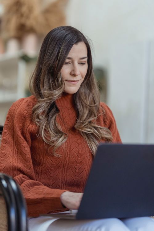 Free Concentrated female freelancer with long hair sitting in armchair and working on netbook during remote workday Stock Photo