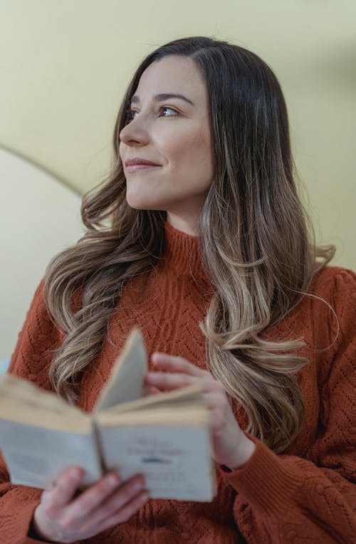 Low angle of positive female with long wavy hair turning page of opened book while reading