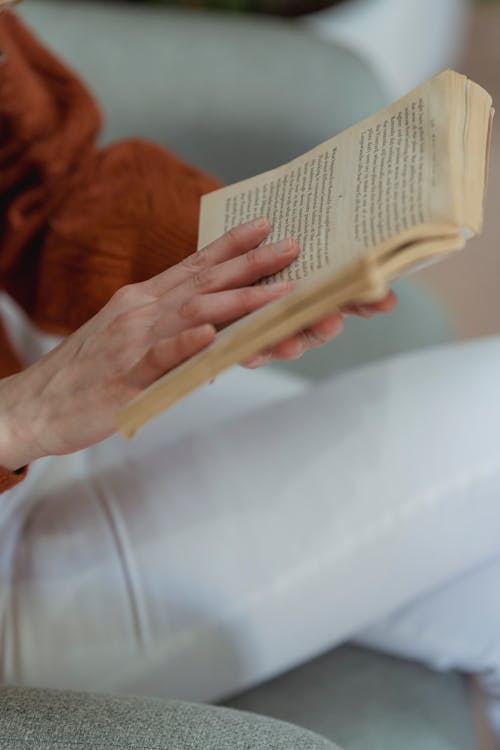 Free High angle of crop anonymous female sitting with crossed legs and reading opened book Stock Photo