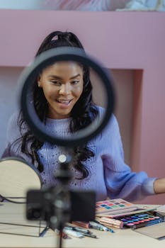 Smiling woman filming a makeup tutorial with ring light and smartphone.