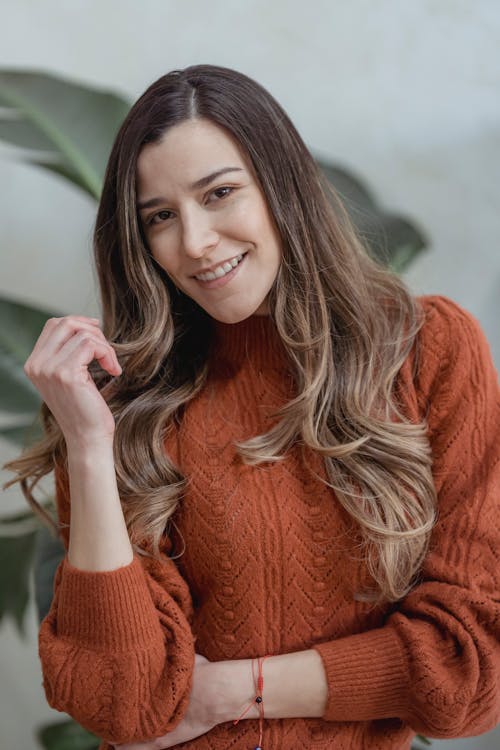 Positive female with long wavy dyed hair wearing warm sweater smiling and looking at camera