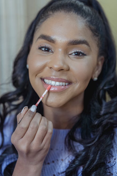 Black woman applying lip gloss during beauty routine