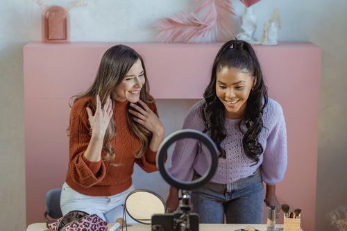 Free Positive multiethnic female makeup artists at table with professional supplies looking at smartphone near ring lamp while recording online lesson Stock Photo