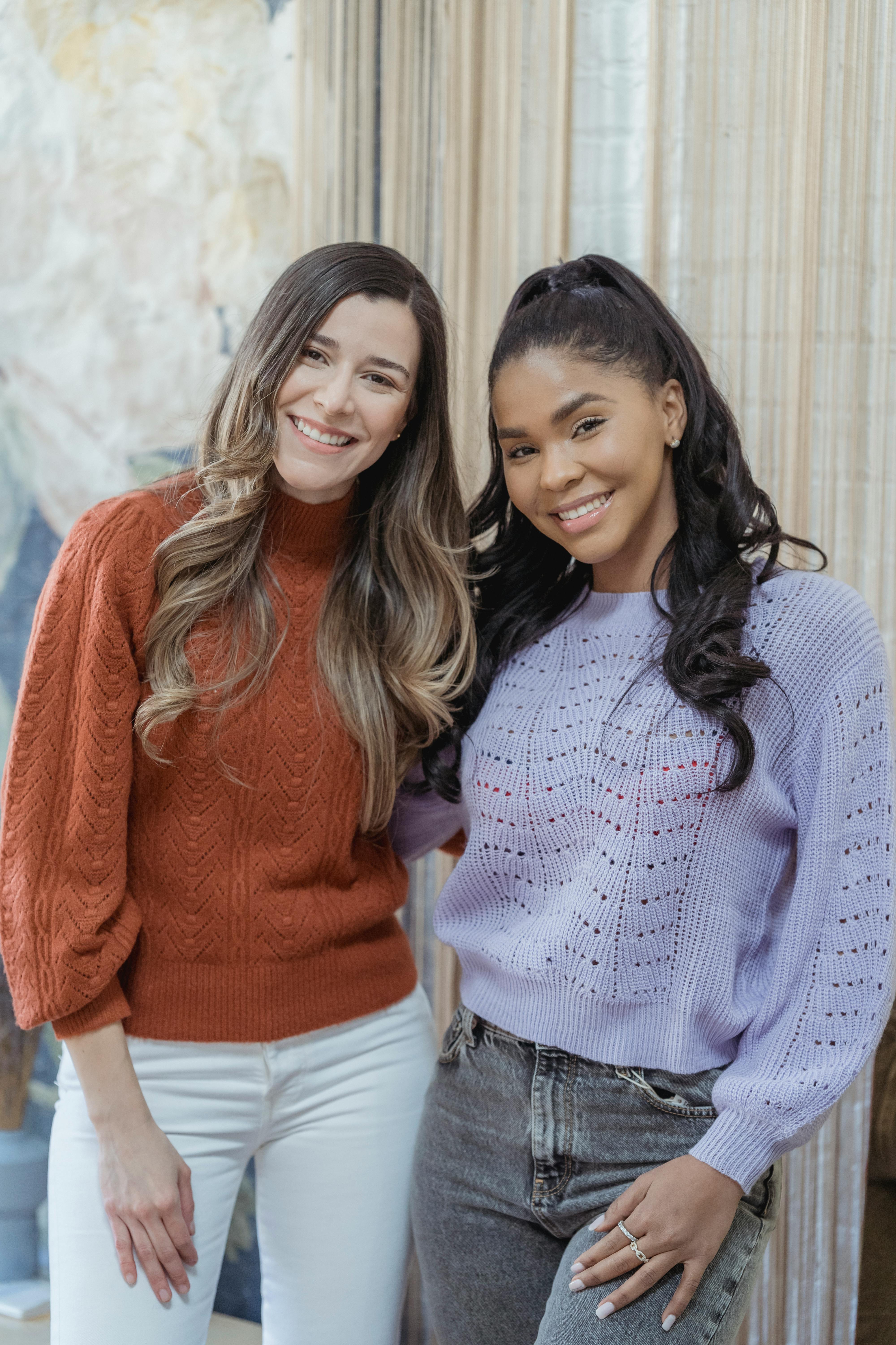 multiethnic glad women with long hair in sweaters smiling