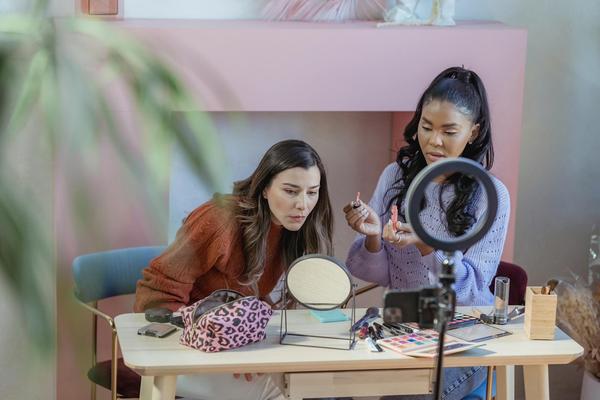 Diverse focused friends at table with eyeshadows and cosmetics near ring lamp in fashion studio