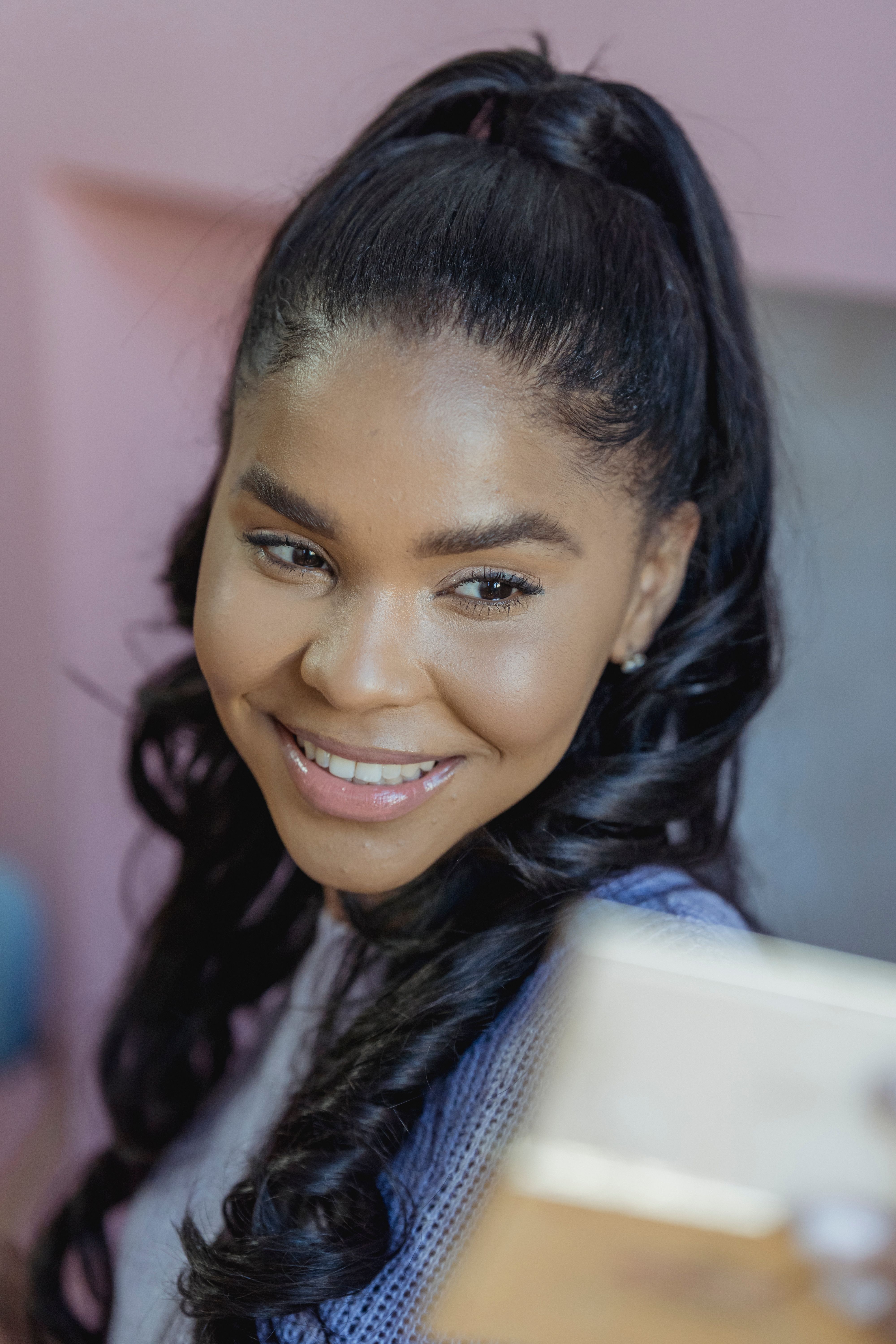 Positive African American female with long hair smiling and looking at mirror on blurred background