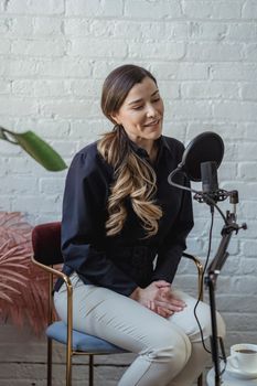 Happy female with long hair speaking and recording voice with professional microphone in studio with white brick walls