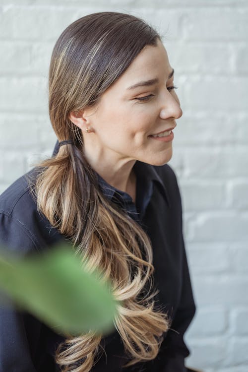 Glad trendy woman with long wavy dyed hair on blurred background of white brick wall