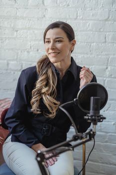 Cheerful female with dyed long hair looking away near microphone and white brick wall of studio
