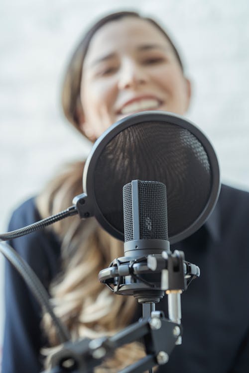 Positive woman smiling and recording audio message with microphone