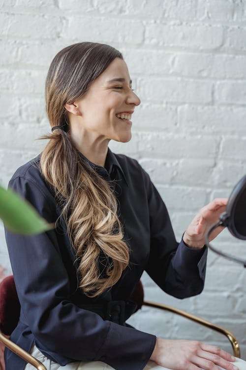 Positive woman with long wavy hair smiling and looking away in studio with brick walls