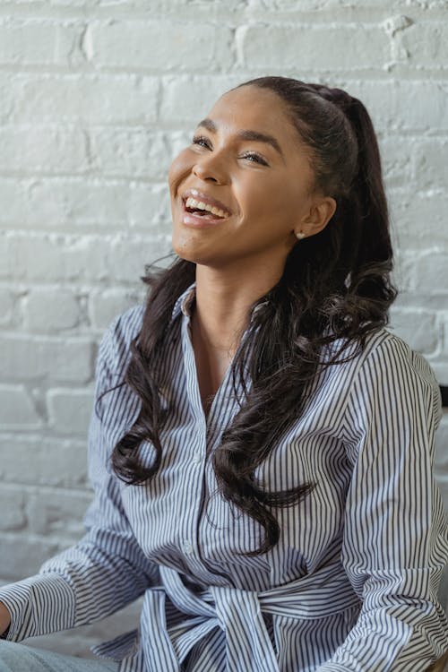 Positive African American female with long wavy hair laughing in modern studio with brick walls