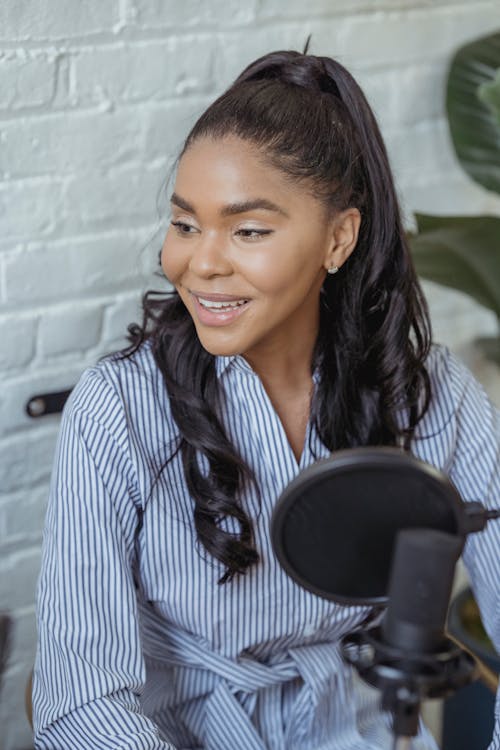 Free Cheerful African American female smiling and recording voice with microphone in contemporary broadcasting studio Stock Photo