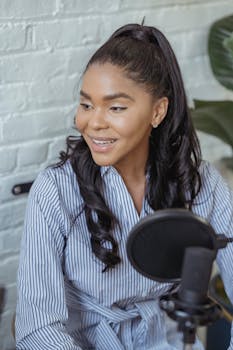 Cheerful African American female smiling and recording voice with microphone in contemporary broadcasting studio