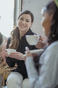 Two women enjoying a friendly conversation while sipping coffee indoors, surrounded by warmth and light.