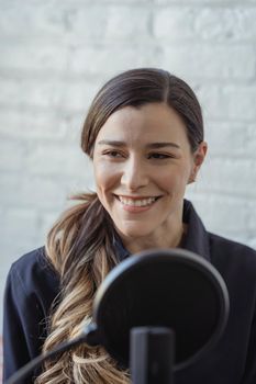 Cheerful female smiling and looking away while recording audio story with microphone in contemporary studio