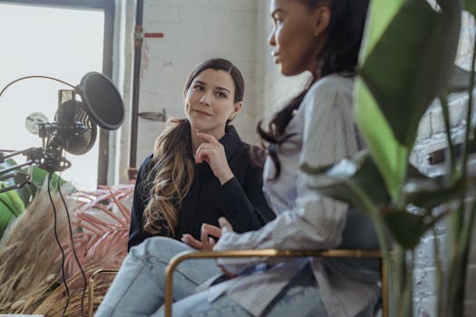 Two women engaging in a podcast conversation indoors with microphone setup.