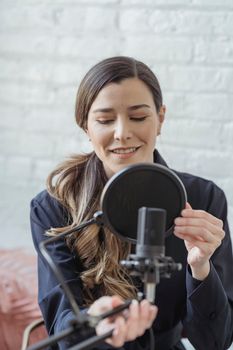Smiling woman in black sweater adjusting microphone for podcast in bright room.