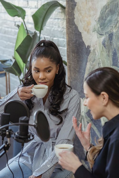 Free Two women enjoy a casual discussion over coffee in a recording studio, embodying togetherness and conversation. Stock Photo