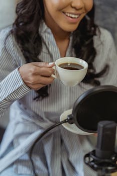 Smiling woman holding coffee in front of a microphone, emphasizing casual content creation.