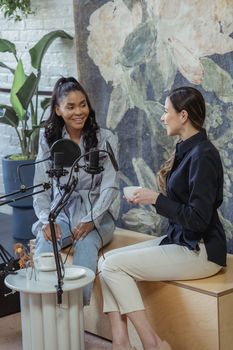 Two women engaged in a casual podcast interview indoors with microphones.