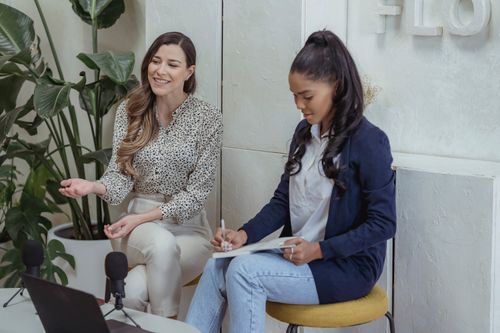 Free Two women engaged in a podcast interview setting, discussing and writing indoors. Stock Photo