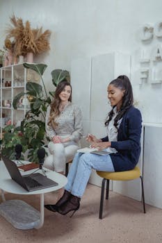 Two women having a professional discussion with microphones and a laptop indoors.