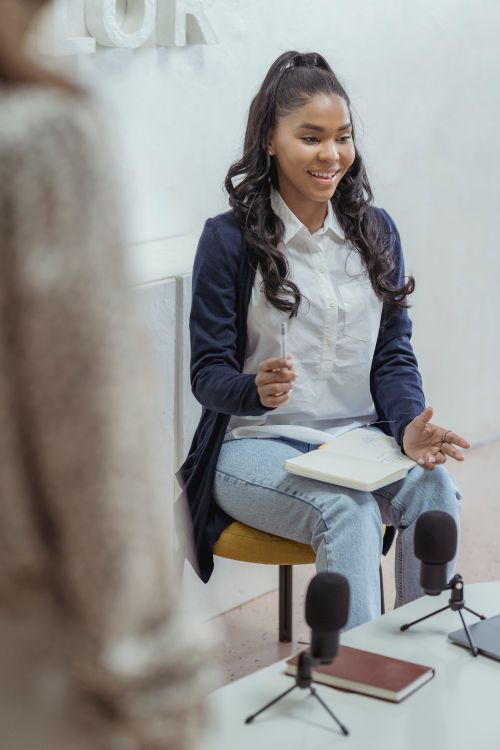 Free Professional woman smiling while engaging in a meeting, taking notes with a notebook and microphones on the table. Stock Photo