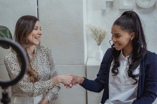 Cheerful multiethnic stylish women smiling and looking at each other in contemporary studio with white walls