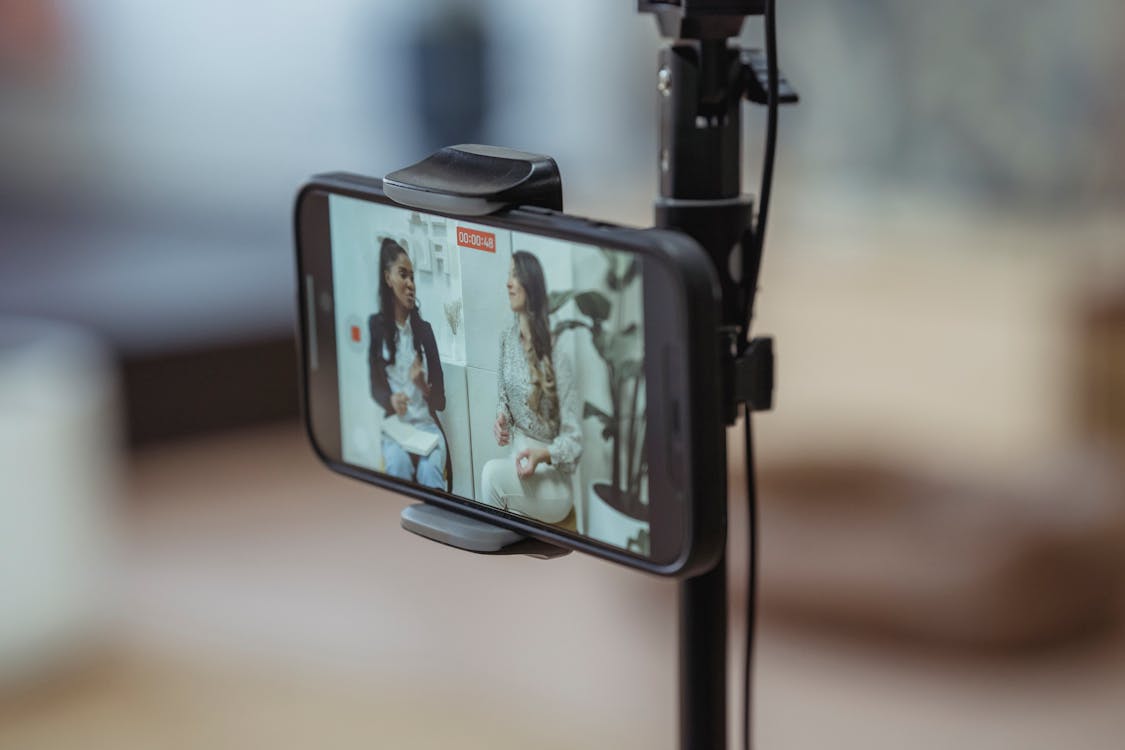 Modern smartphone on tripod recording video of content stylish women having friendly conversation