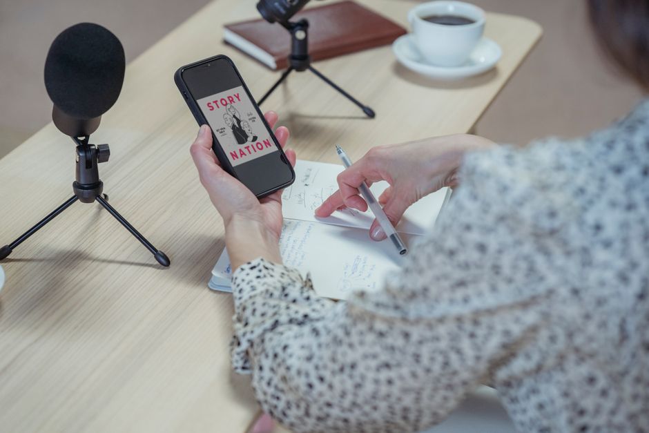 블로그 에드센스 수익화: 초보도 월 100만원 달성 전략 13 A woman records a podcast at a desk using a smartphone and microphones.