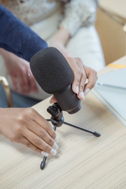 Free From above of crop anonymous female putting microphone on wooden table while recording podcast colleague in studio Stock Photo
